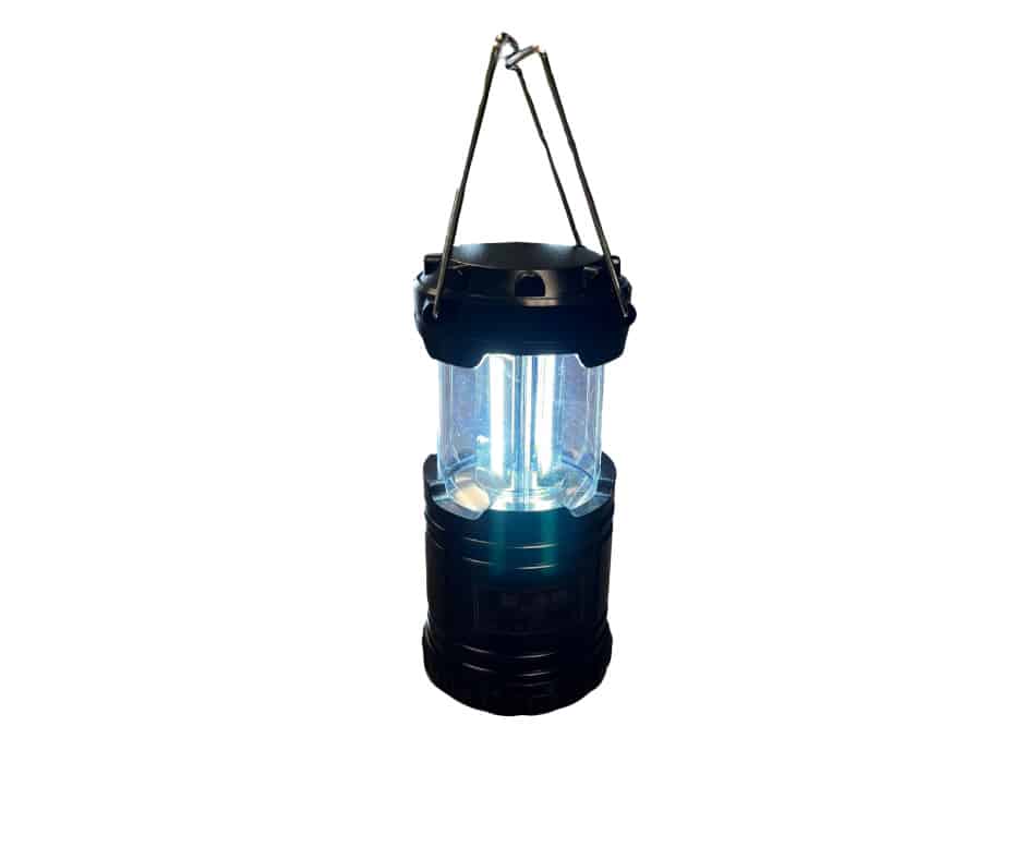 Compact LED camping lantern with telescoping design and metal hanging handles, turned on and glowing bright.||